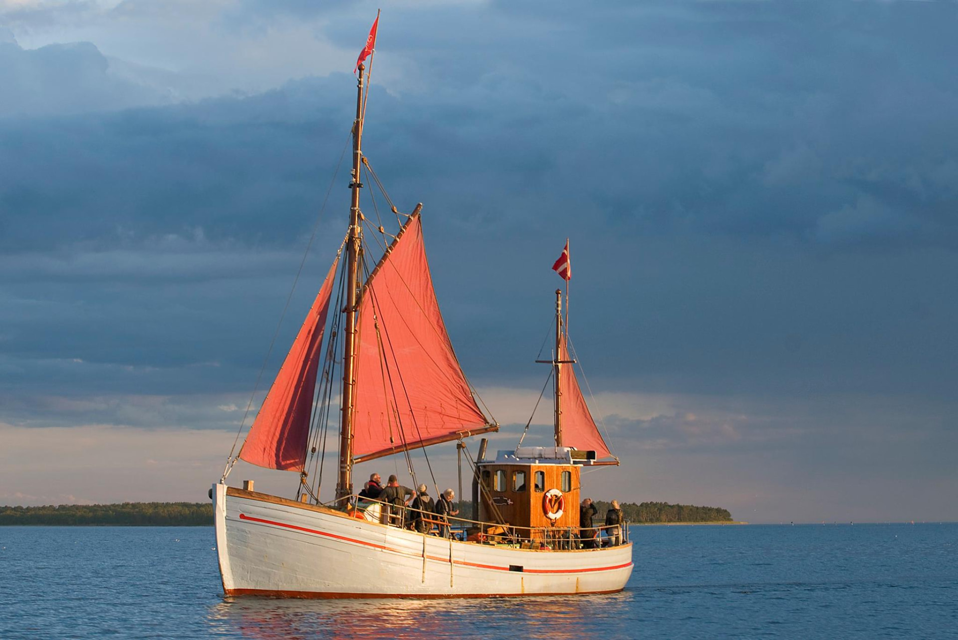 Ålekvasen Rigmor for røde sejl på roligt vand i aftensol med gæster om bord